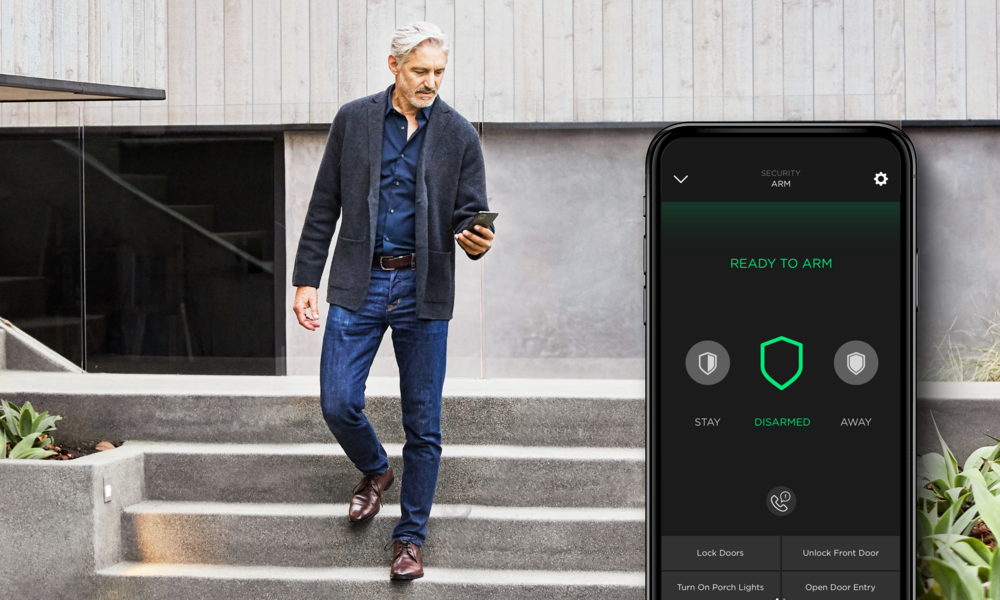 <span class="uk-h4">A man checking his smart home security app while walking down the stairs outside his home.</span>
