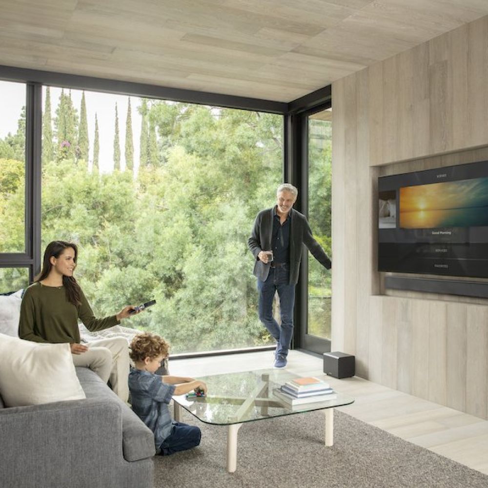<span class="uk-h4">A woman sitting at a couch next to a young boy with a man standing next to a window nearby.</span>