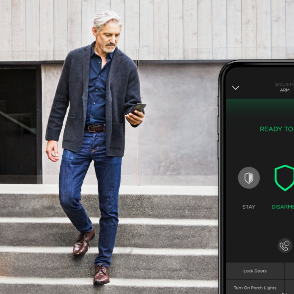 <span class="uk-h4">A man checking his smart home security app while walking down the stairs outside his home.</span>