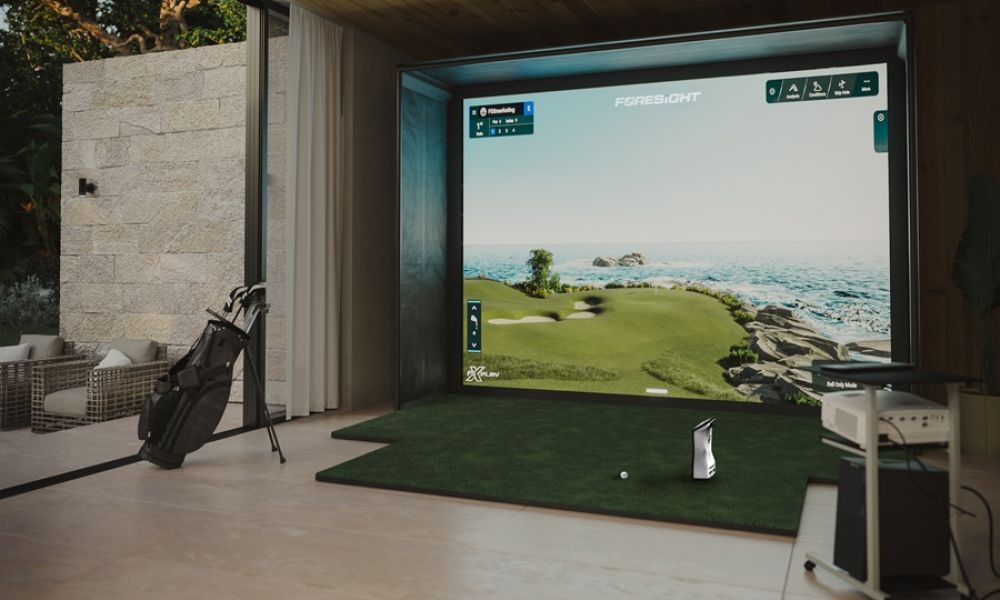 <span class="uk-h4">Foresight Sports golf simulator with ocean-course screen, putting turf, and golf bag in a home entertainment room</span>